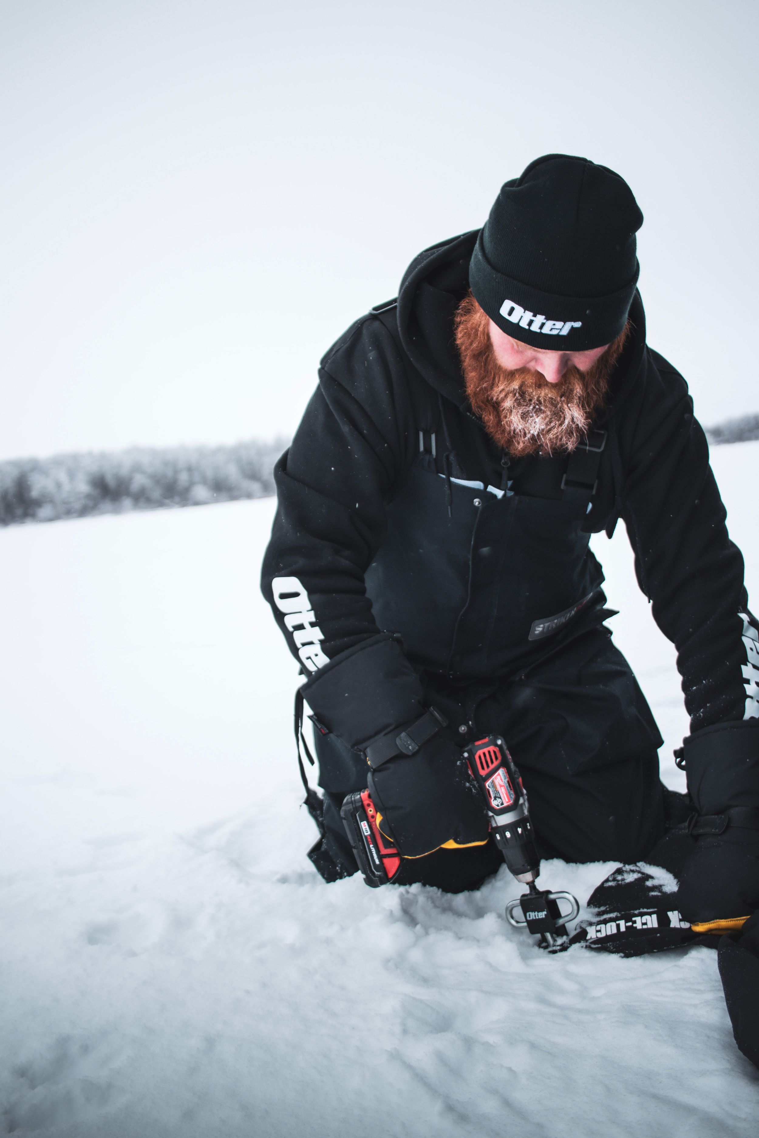 Winter ice fishing scene with person in dark clothing kneeling on frozen lake.