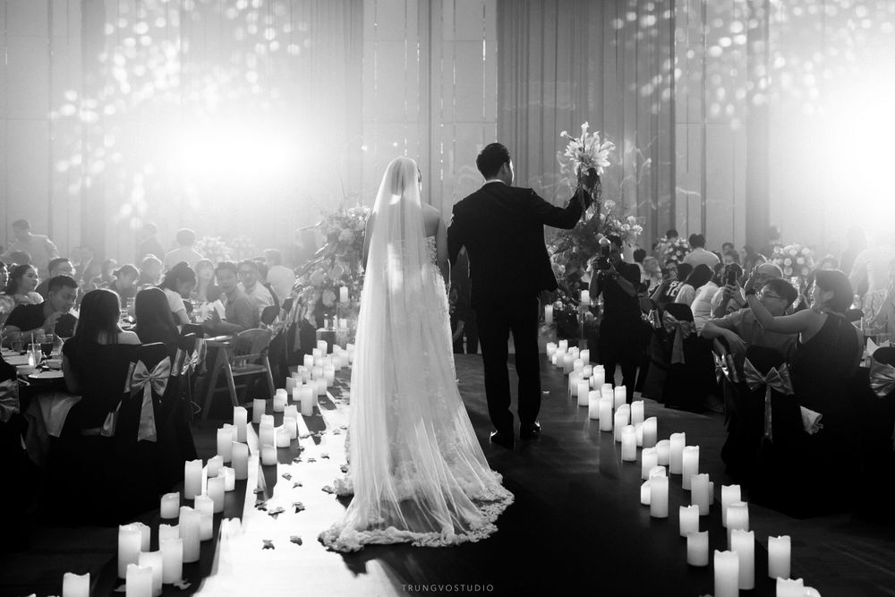 Black and white wedding photo of couple walking down candlelit aisle before seated guests.