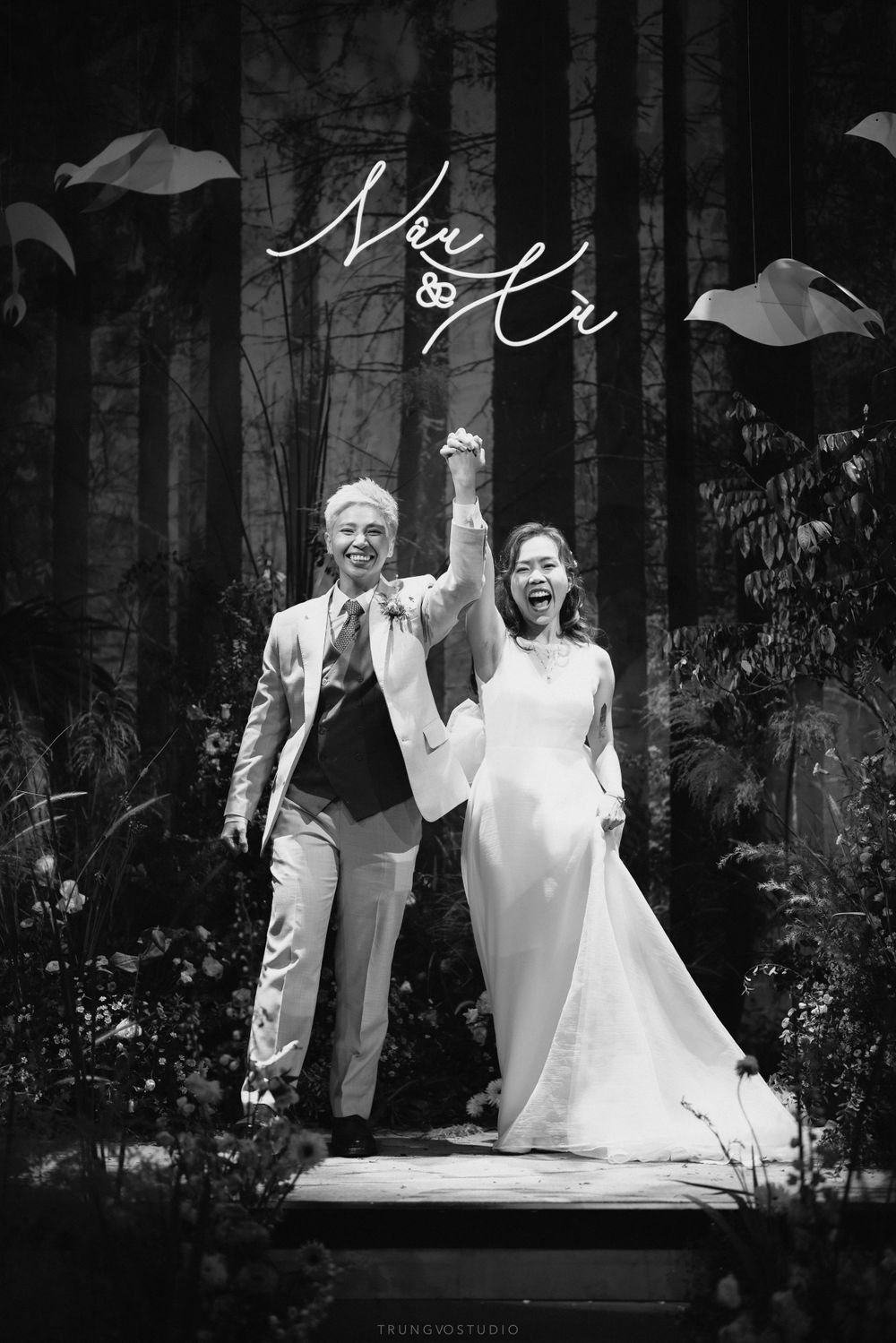 Bride and groom celebrating with raised hands in a black and white wedding portrait.