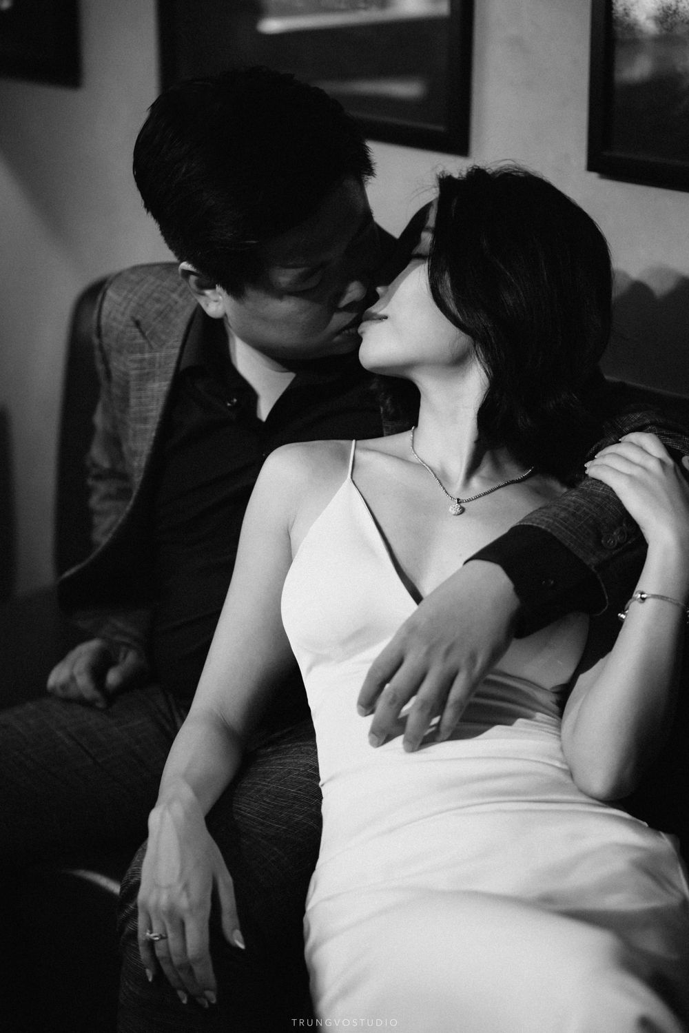 Romantic black and white photo of couple sharing a kiss while seated together intimately.