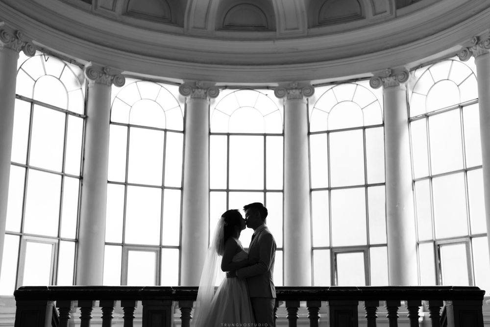 Black and white silhouette of couple kissing in elegant rotunda with tall arched windows.
