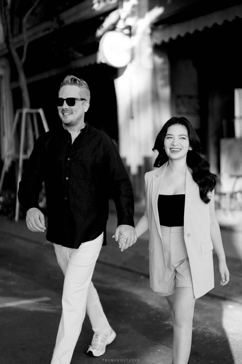 Black and white photo of smiling couple holding hands walking together on a street at night.
