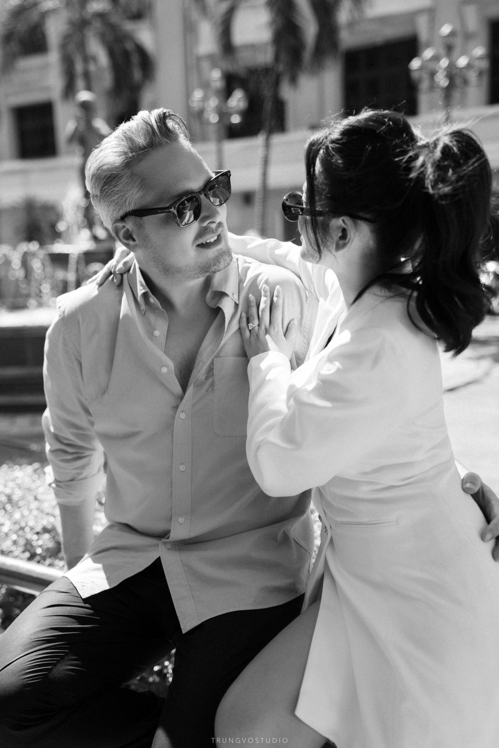 Black and white photo of laughing couple wearing sunglasses sharing a joyful outdoor moment.