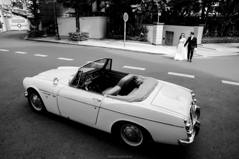 Classic white convertible car on city street with bride and groom in background, black and white.