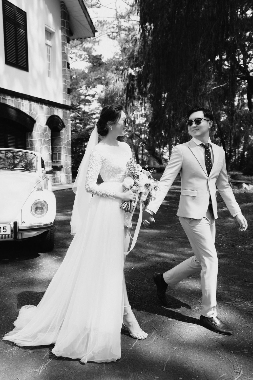 Bride and groom walk hand in hand past vintage Volkswagen Beetle, black and white wedding portrait.