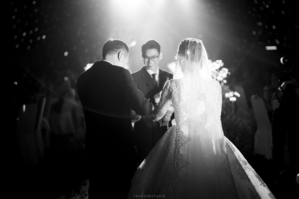Black and white photo of a bride and groom exchanging vows with an officiant during a dramatic wedding ceremony.