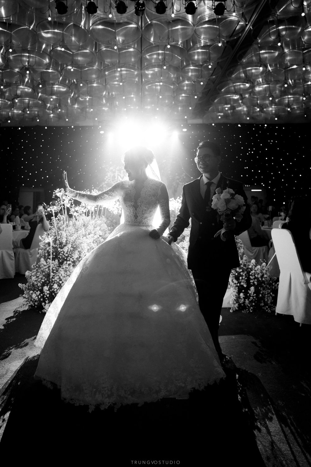 Bride in a voluminous ball gown and groom making a grand entrance at a wedding reception in black and white.