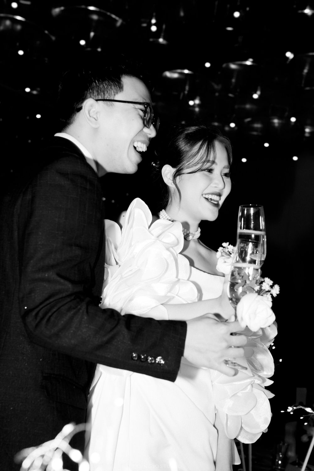 Joyful bride and groom laughing and toasting with champagne glasses at their wedding reception celebration.