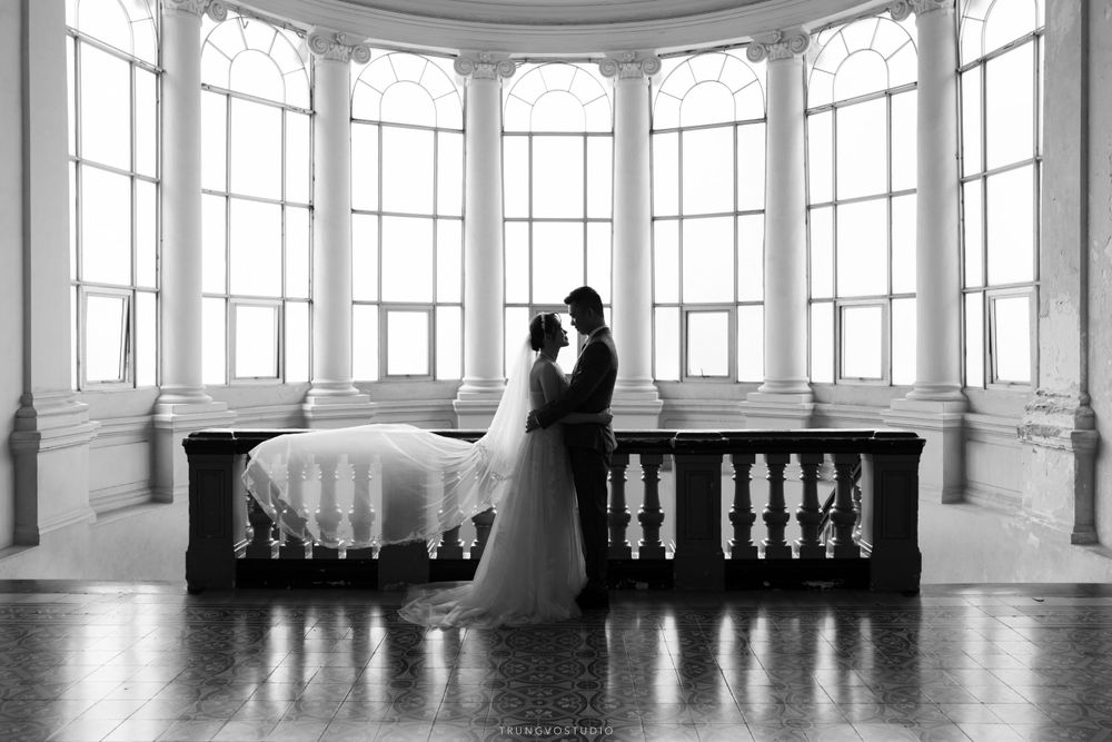Black and white silhouette of a bride and groom embracing near large arched windows.