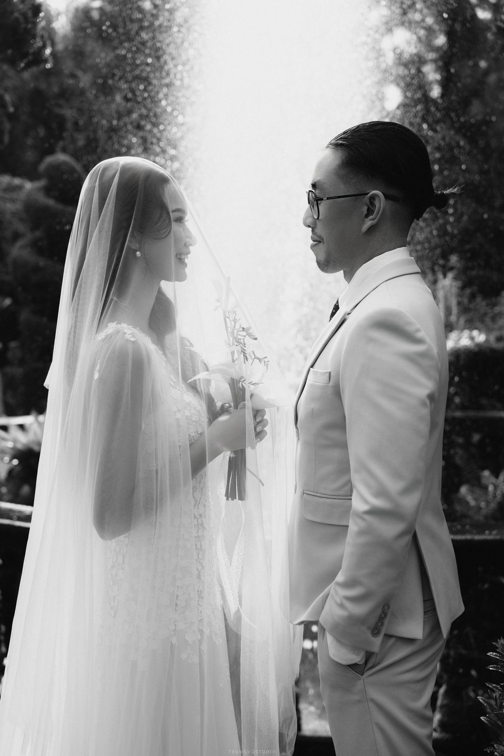 Bride and groom sharing intimate moment holding hands near fountain, black and white wedding photography.