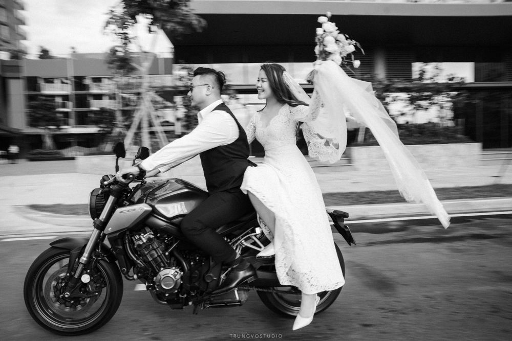 Dynamic black and white photo of a bride and groom riding a motorcycle with veil flowing in wind.