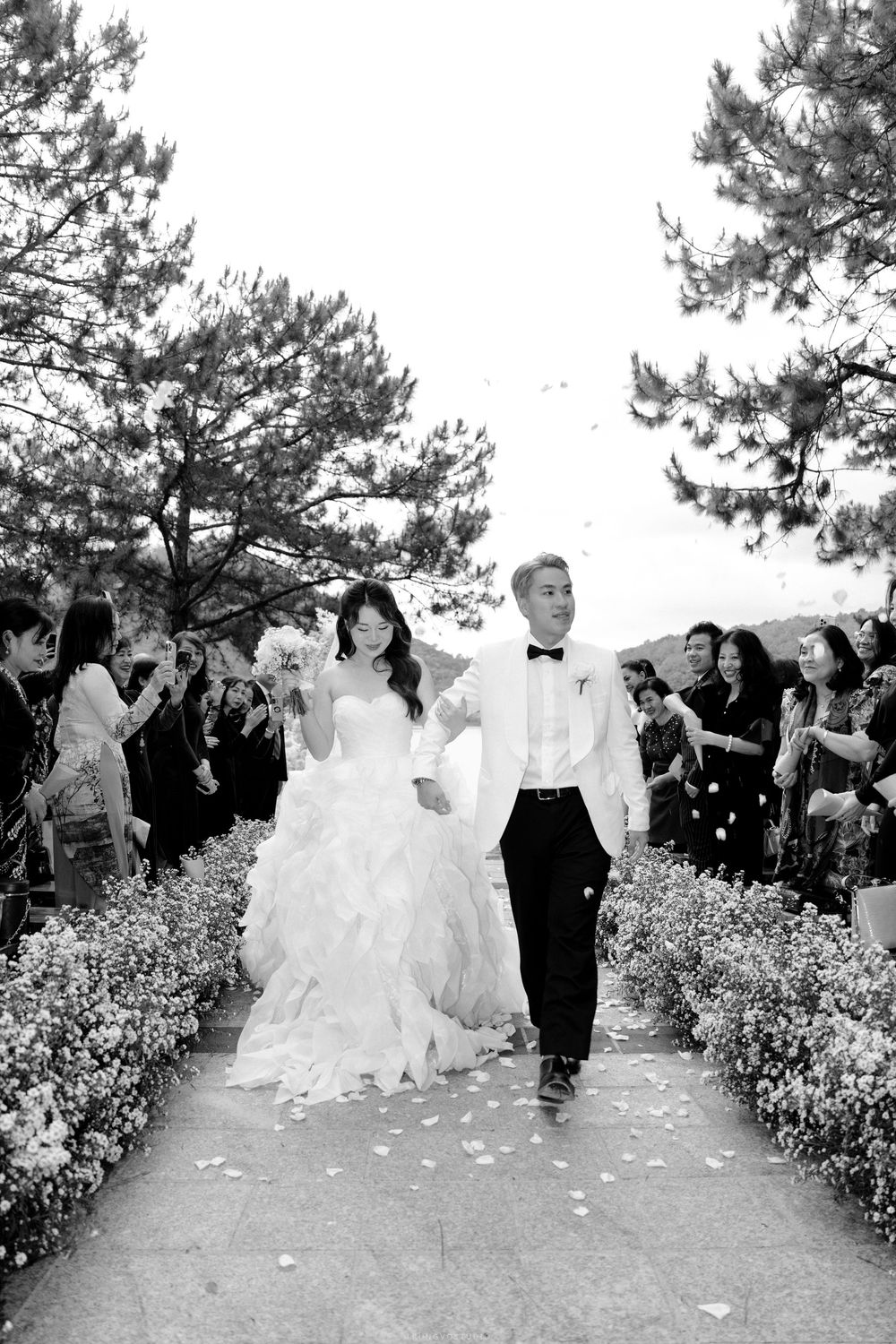 Black and white photo of newlyweds walking back down the aisle as guests celebrate with petals.