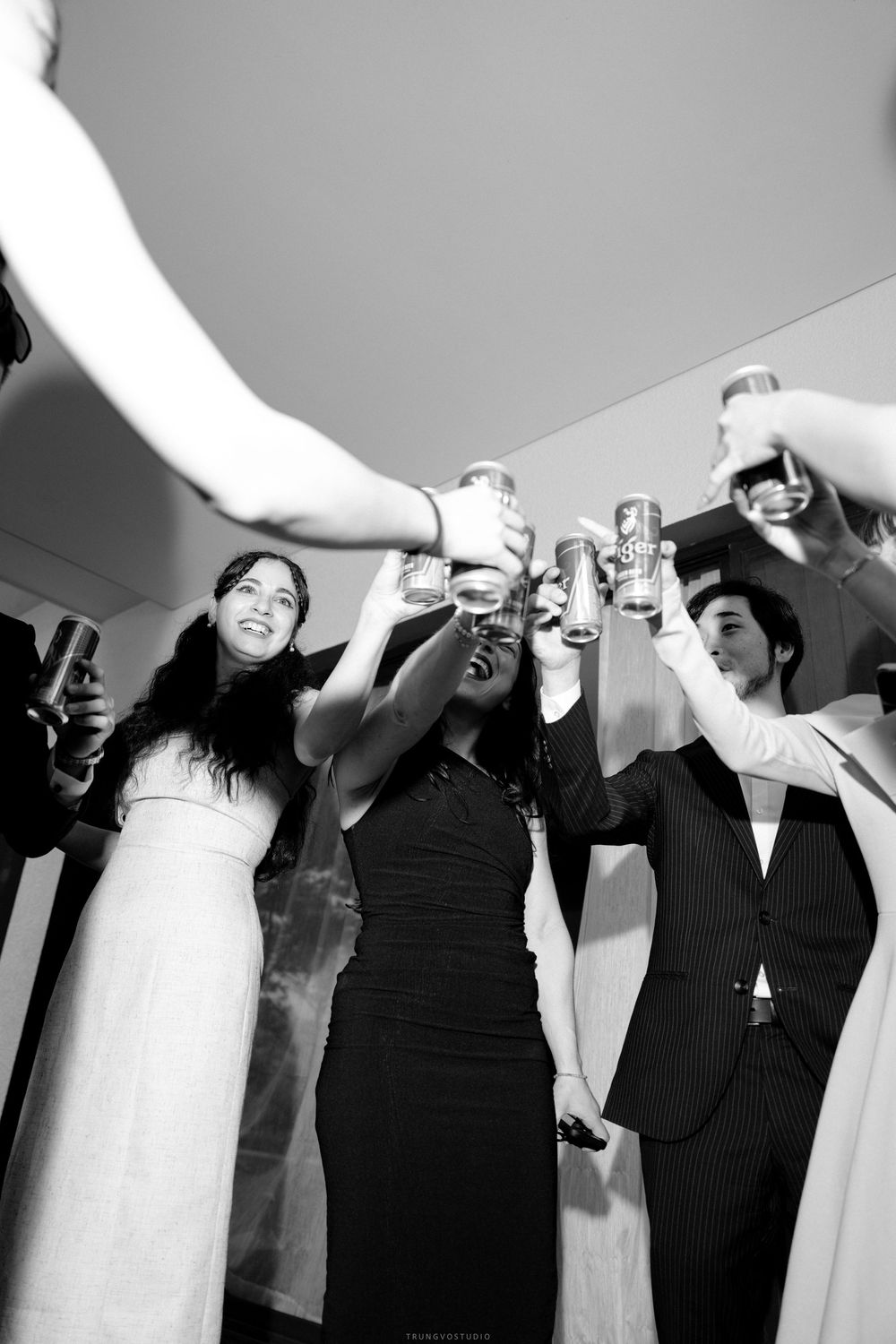 Black and white photo of wedding guests raising glasses in a celebratory toast at a reception.