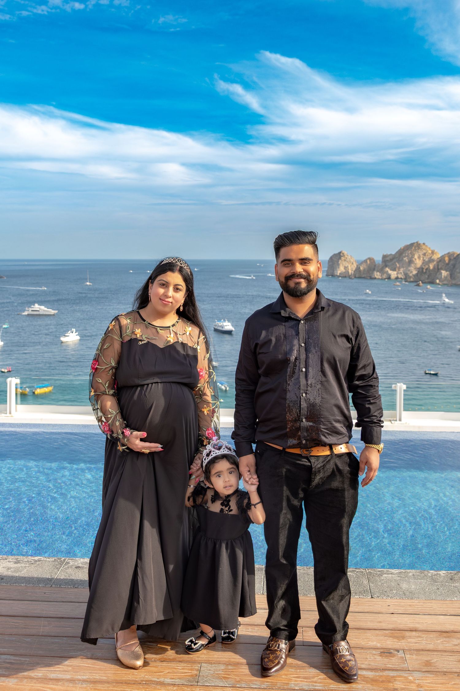 A family poses on a wooden deck overlooking the ocean and rock formations at a scenic coastal destination.