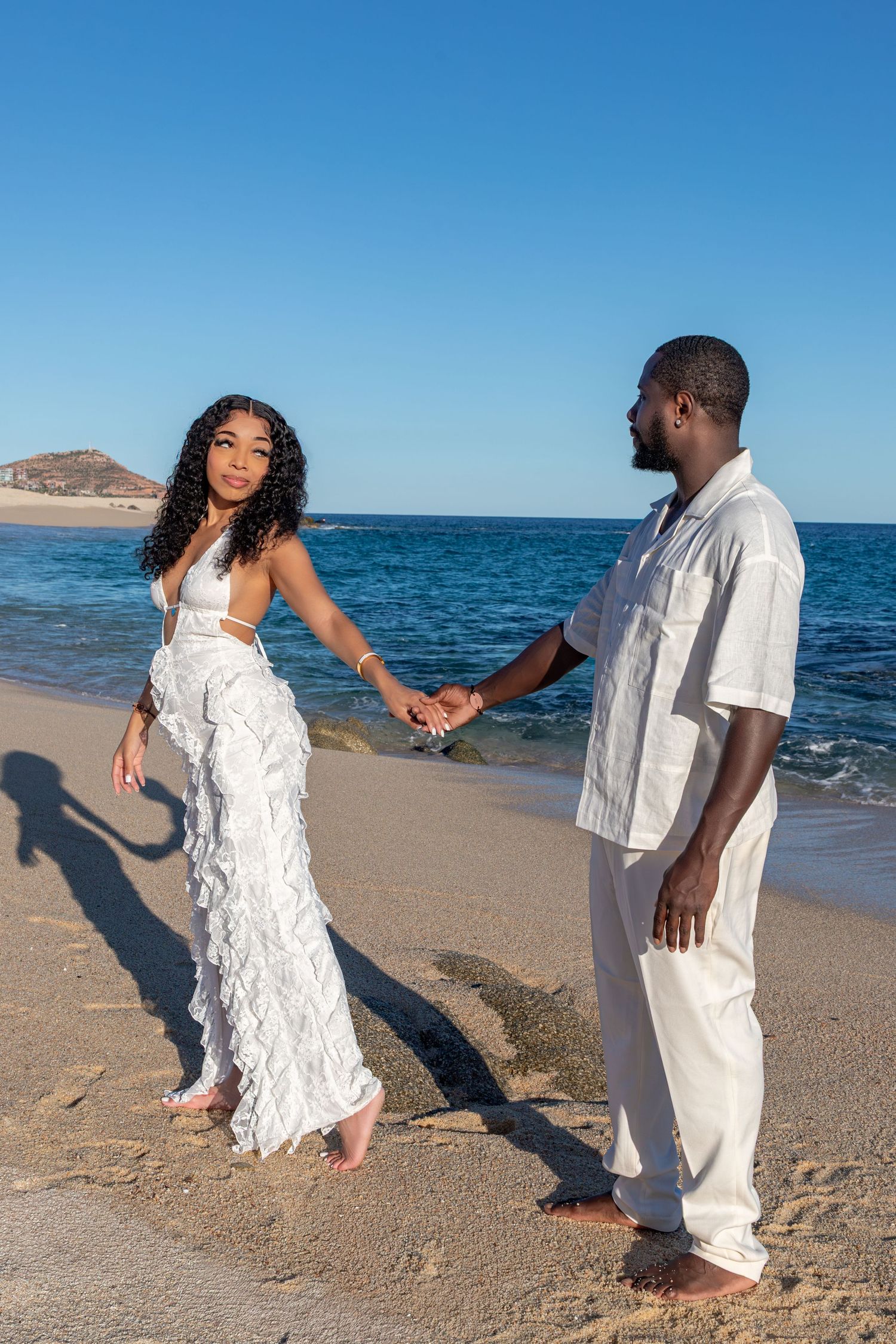 A couple dances together on a scenic beach with blue ocean waters and clear skies in the background.