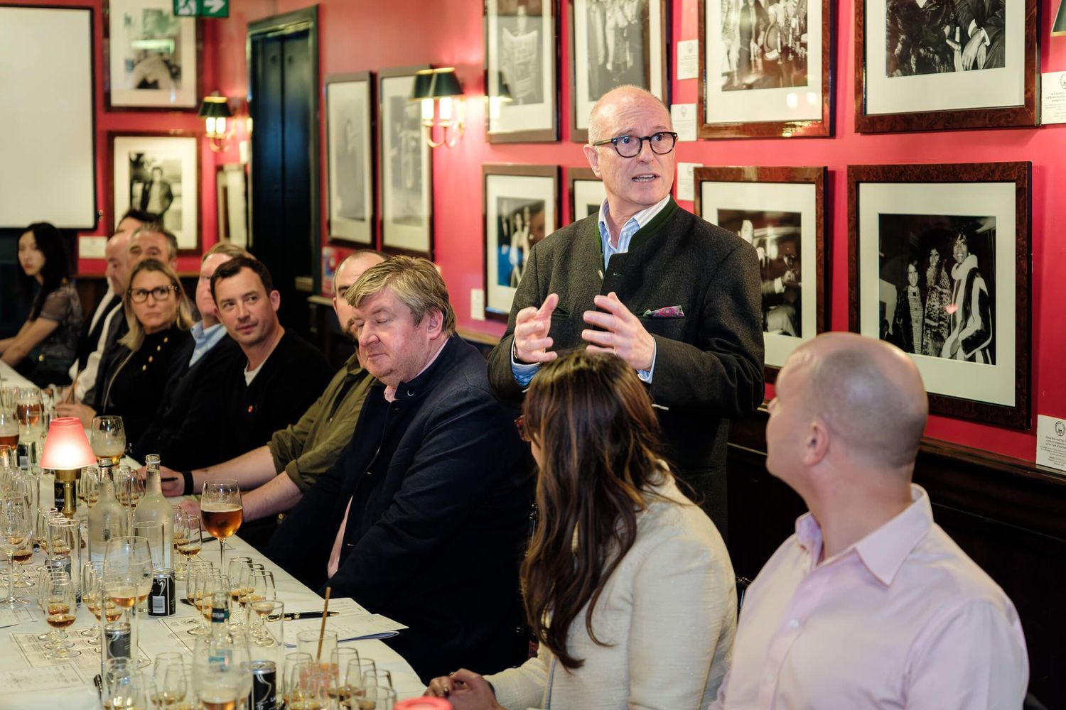 People gather at a restaurant table with red walls and framed photographs displayed in the background during a social event.