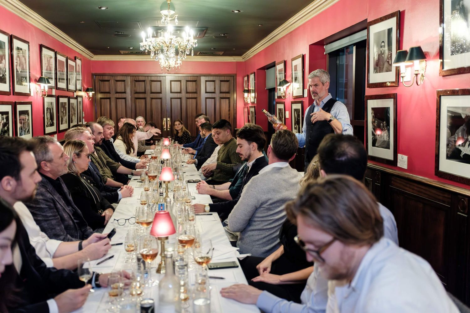 Panoramic view of a formal dining room with pink walls, chandeliers and guests seated at long tables for a special event.