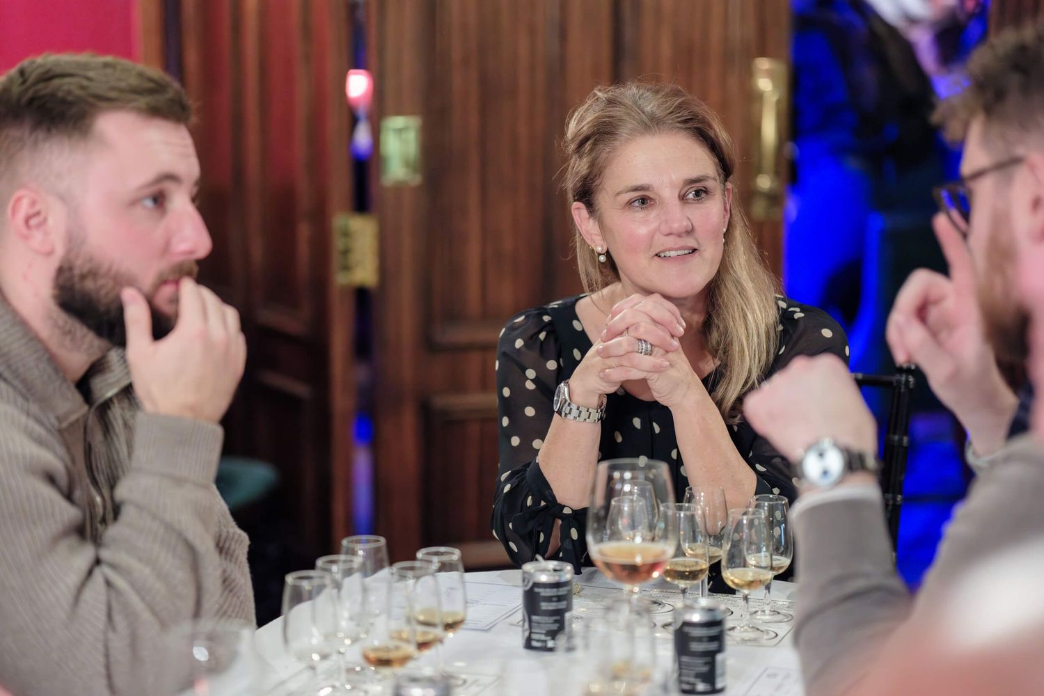 People gathered at dining tables participate in what appears to be a wine tasting event in an upscale venue.