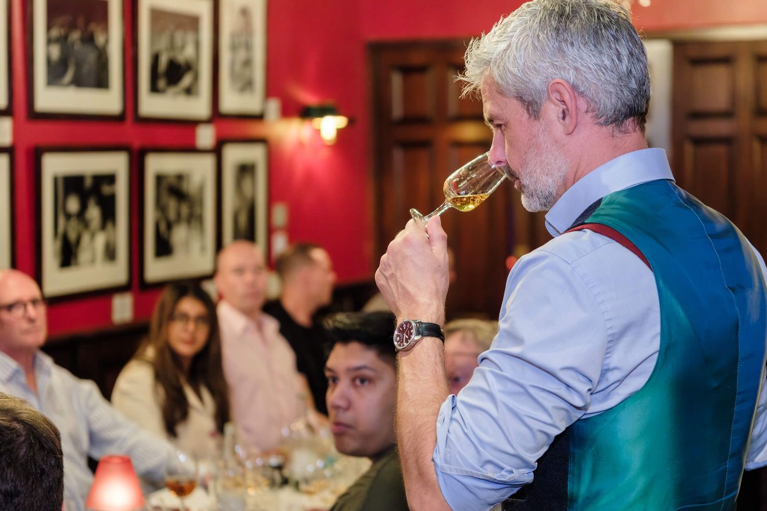 Diners in business attire participate in a wine tasting event at an upscale restaurant with red walls.