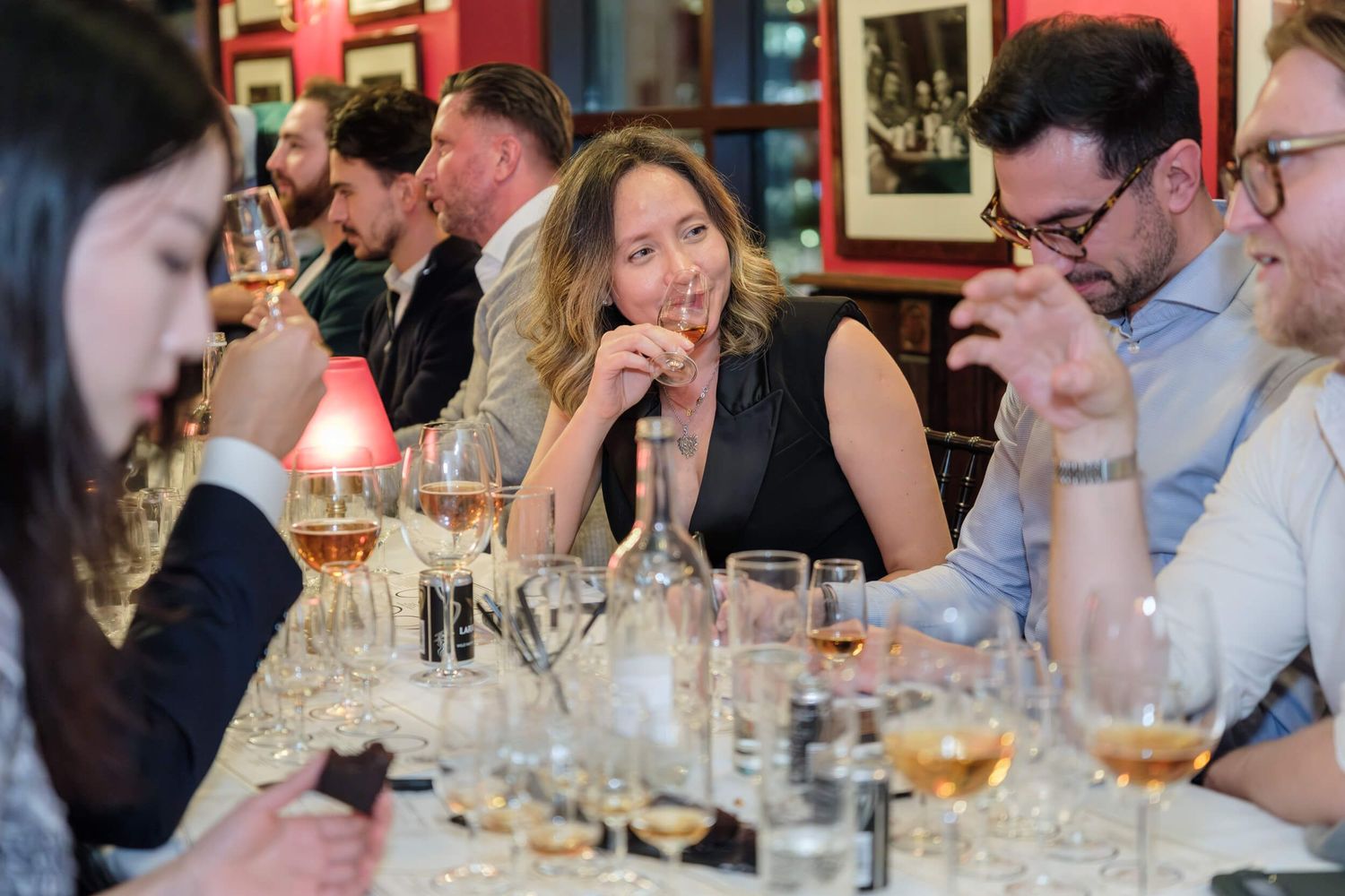 Guests engaged in lively conversation around a dining table with wine glasses and warm lighting at a social gathering.