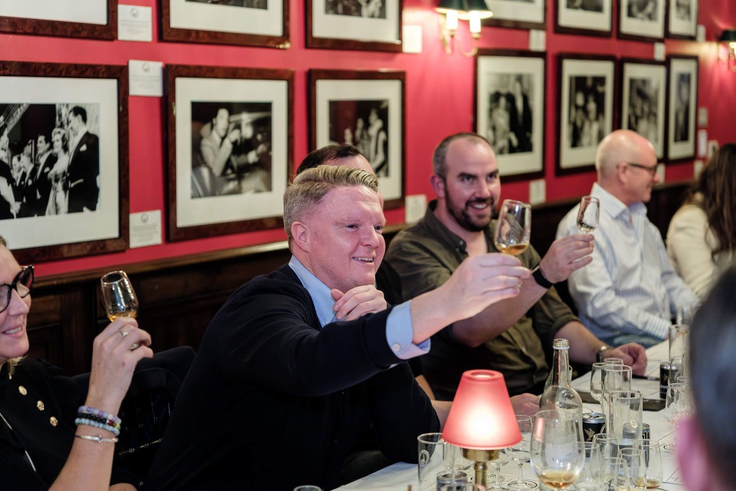 People gathered at a restaurant table with red walls decorated with black and white photographs in the background.