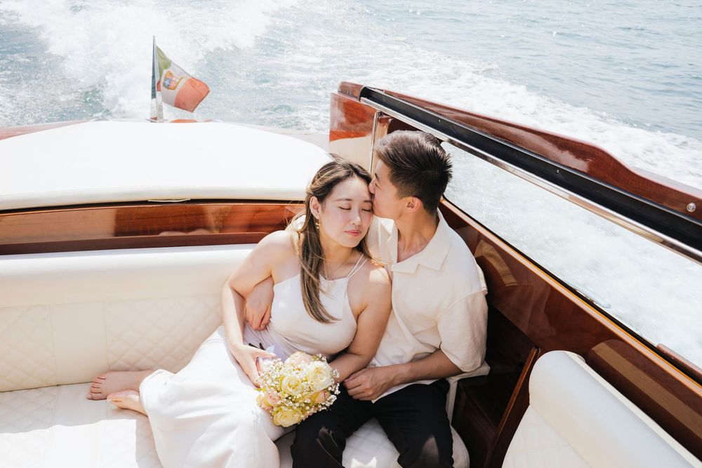 A romantic couple shares an intimate moment while riding in a luxurious wooden boat on the water.