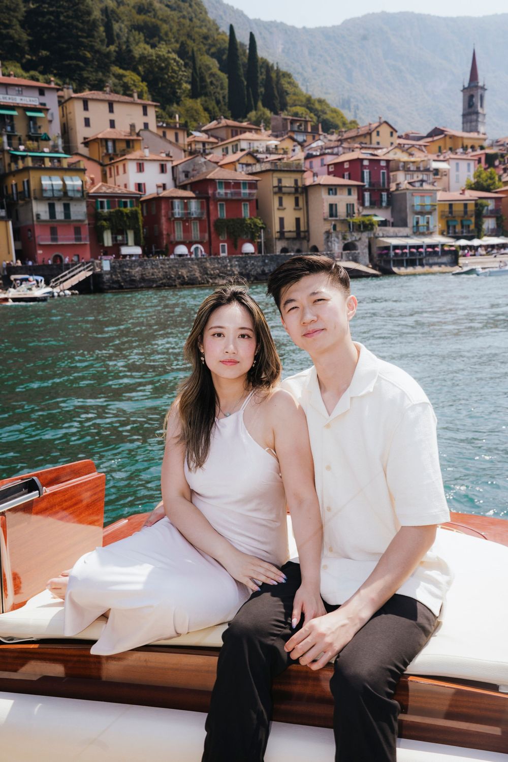 A couple relaxes on a wooden boat while touring the colorful waterfront buildings of an Italian lakeside village.