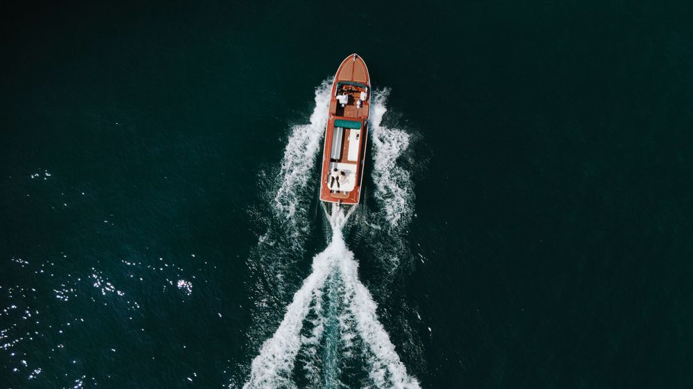 Aerial view of a red and white speedboat cutting through dark blue ocean waters creating a dramatic wake pattern.