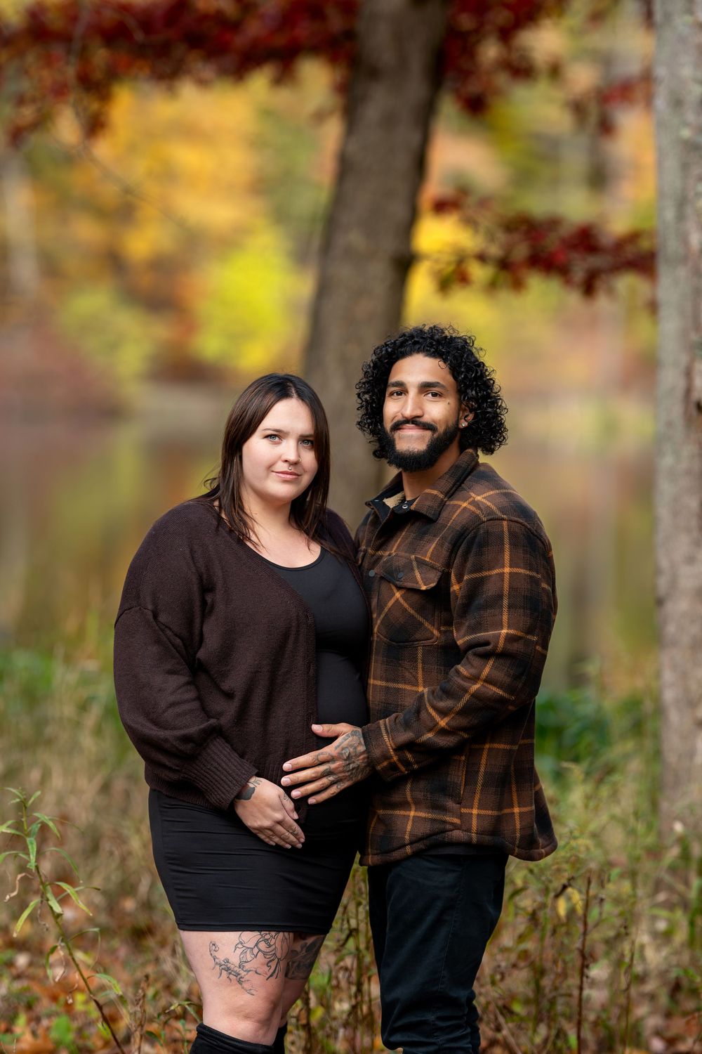 Expecting couple holds baby bump together in a stunning autumn forest setting with colorful fall foliage.