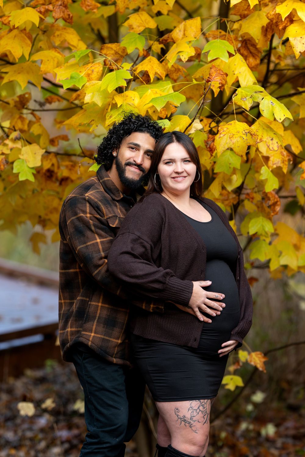 Couple embracing under vibrant yellow autumn maple tree during outdoor maternity photo session.