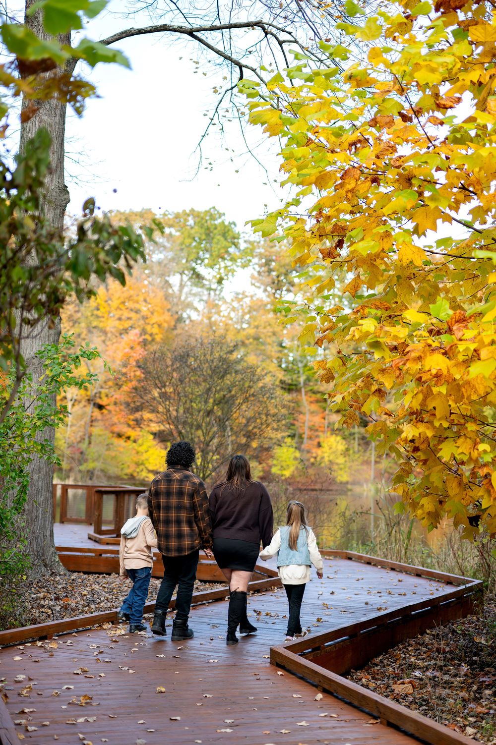 Family walking on a wooden boardwalk path surrounded by colorful fall foliage.