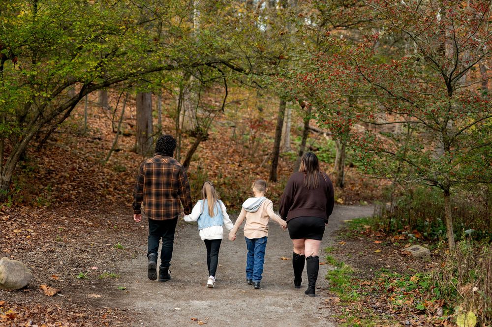 Family of four walking away on a forest path surrounded by fall foliage.