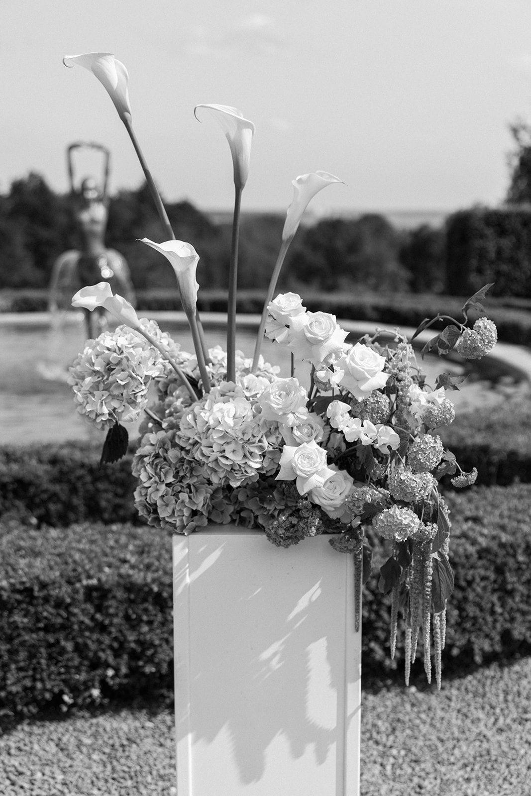 Black and white photograph of white floral arrangements in vases displayed outdoors with a garden backdrop.