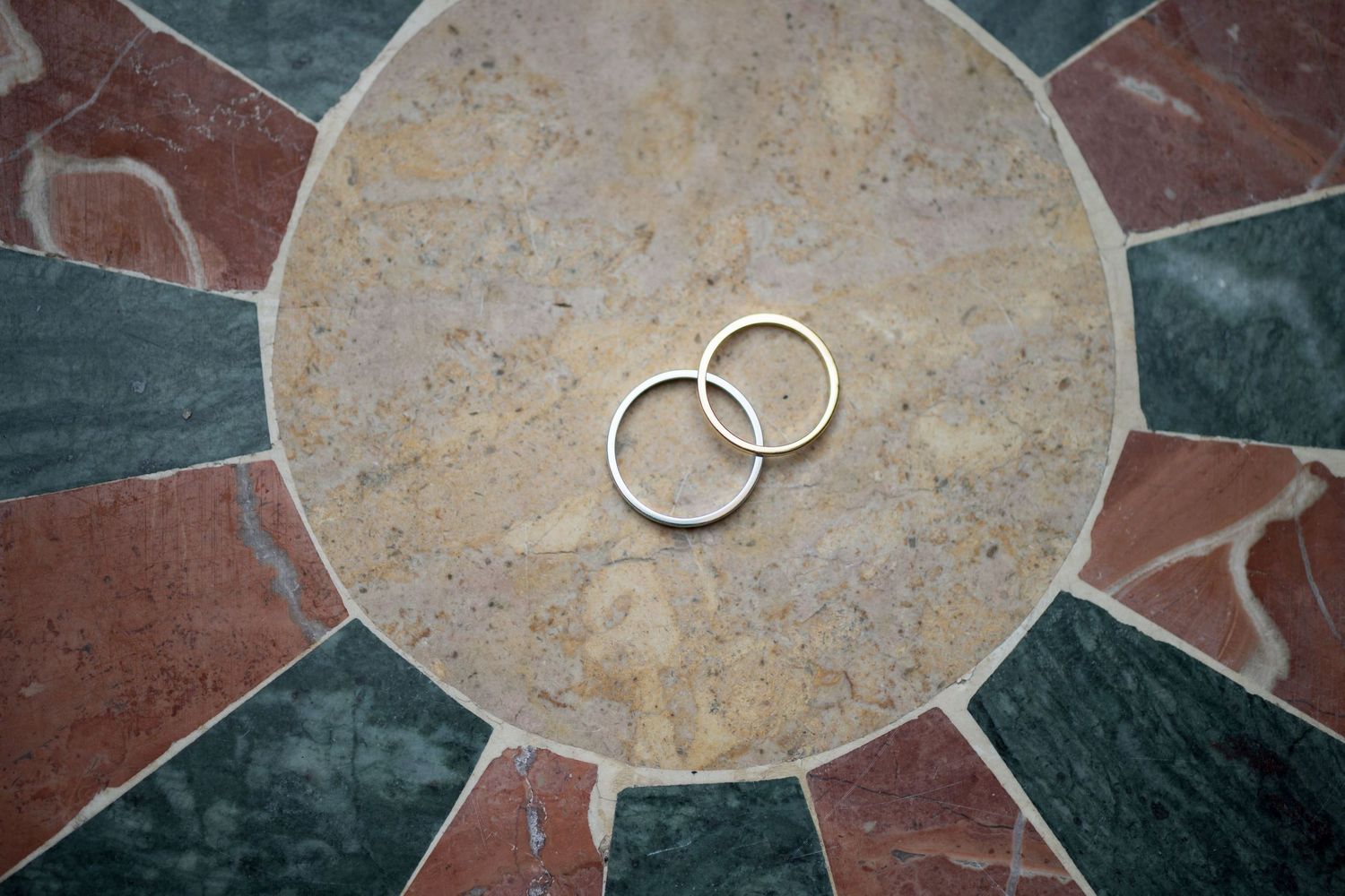 Photo artistique des alliances posées sur un sol en pierre circulaire, détail élégant et symbolique du mariage.