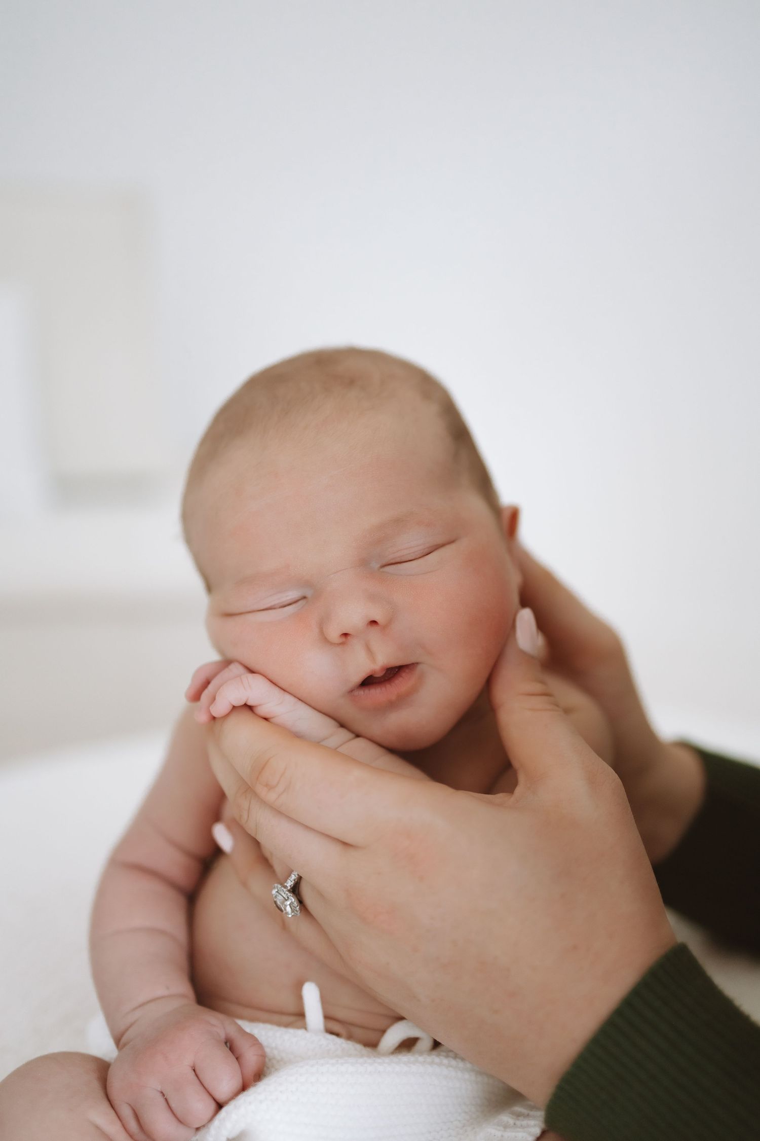 A sleeping newborn baby swaddled in white blankets being gently held in someone's hands.