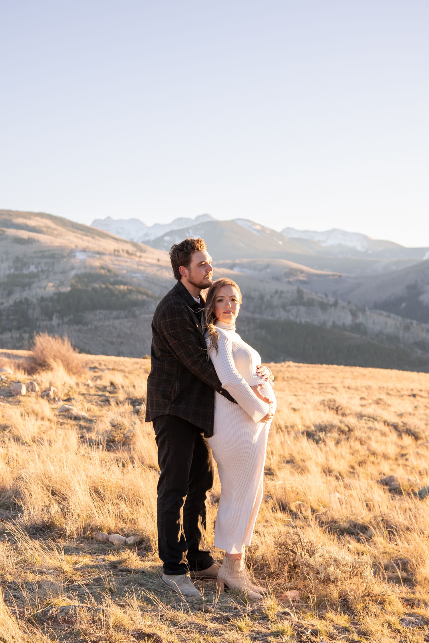 A couple embraces during a golden hour photo session in the mountains for a moody and editorial maternity photo session in Vail Colorado