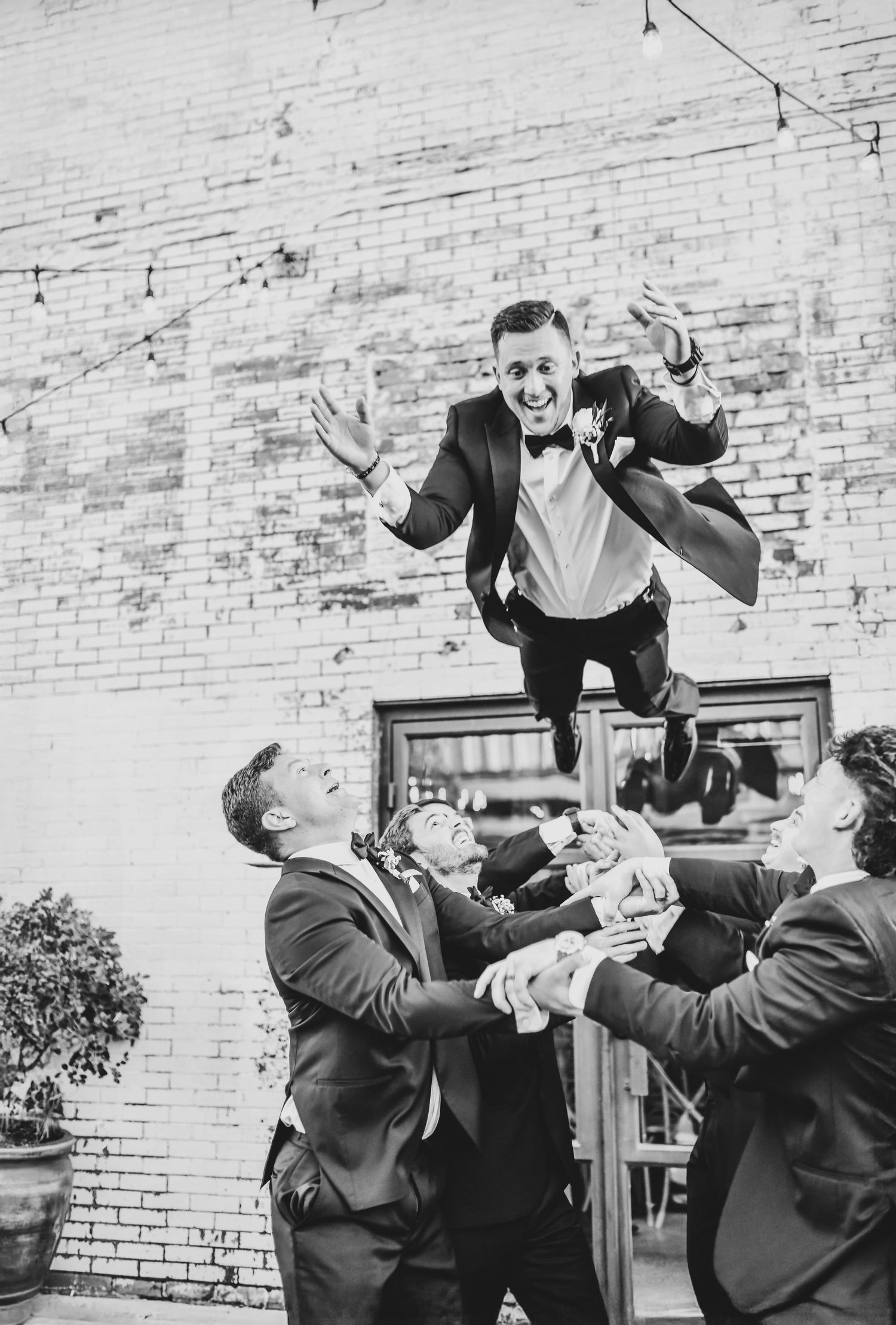 Groom tossed into the air by his groomsmen in a joyful celebration shot, editorial-style with warehouse textures behind them.