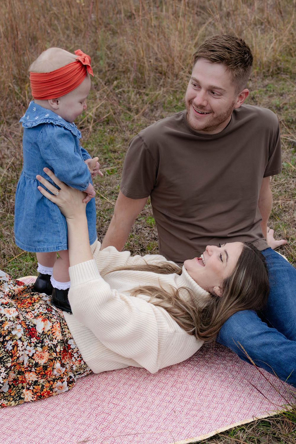 True West Photography - Family relaxes together on a pink picnic blanket in a rustic outdoor setting.