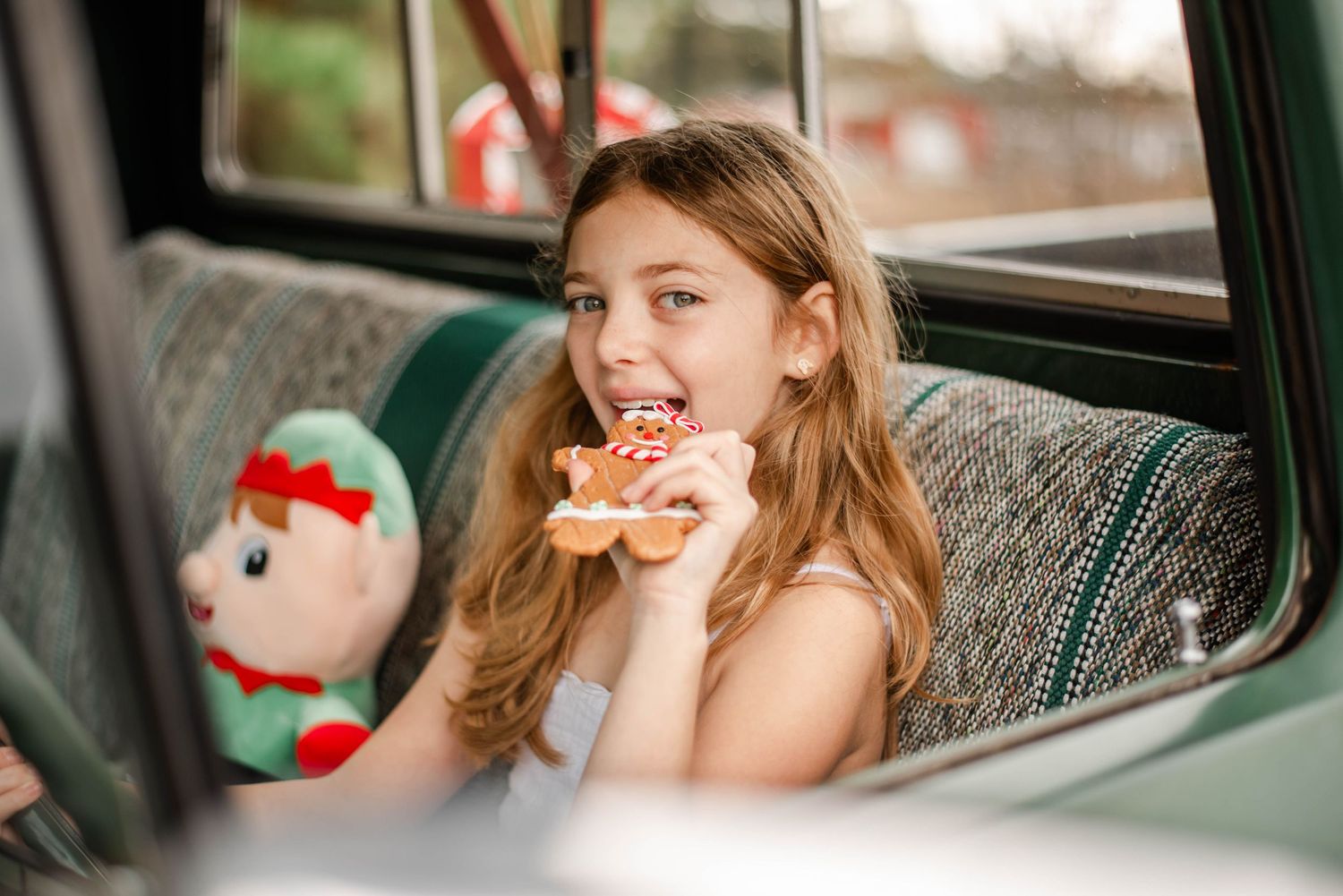 A person sits in a car backseat with a stuffed snowman plush toy visible in the background.