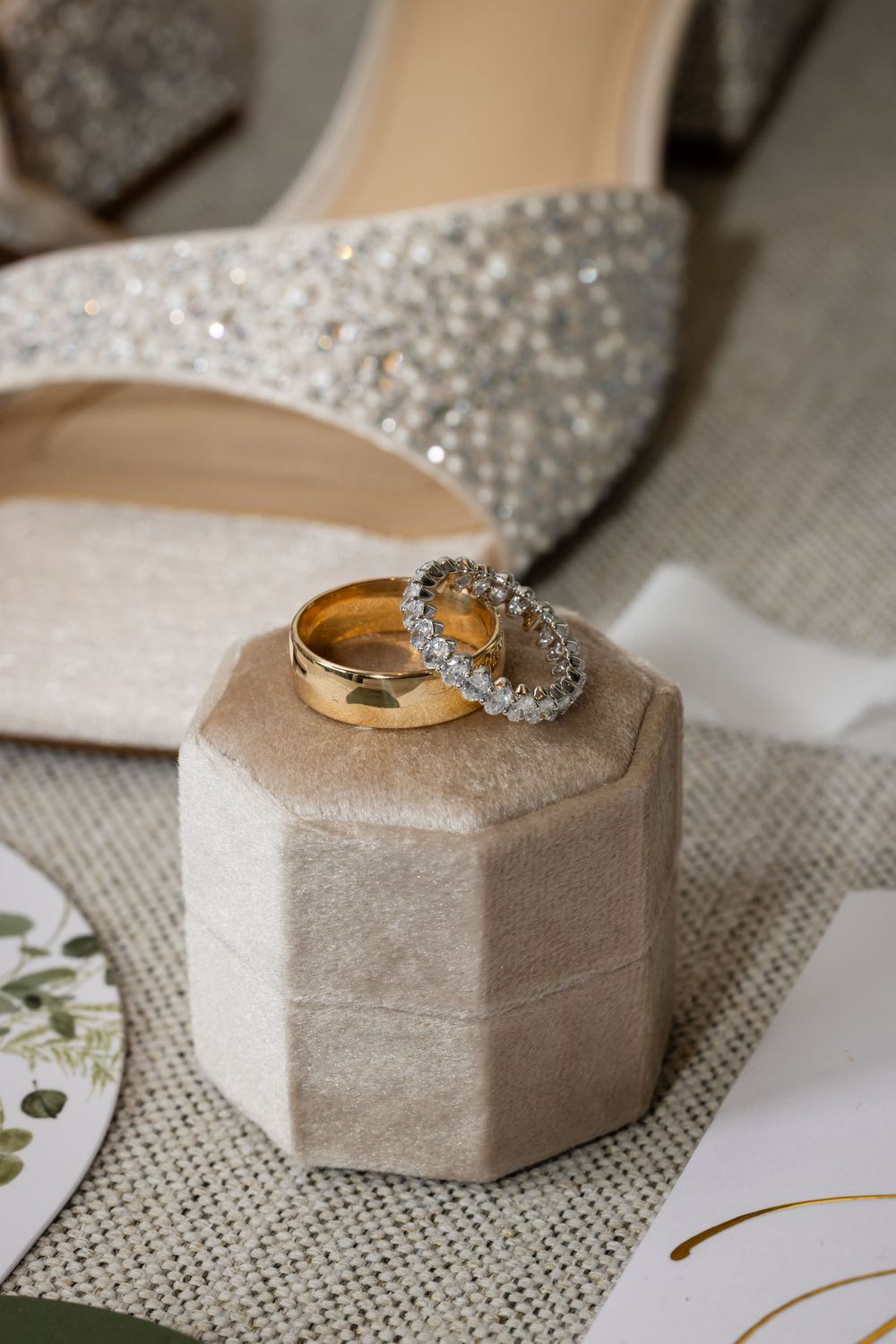 Wedding rings displayed on a textured velvet ring box with a sparkly diamond band and gold band on neutral background.