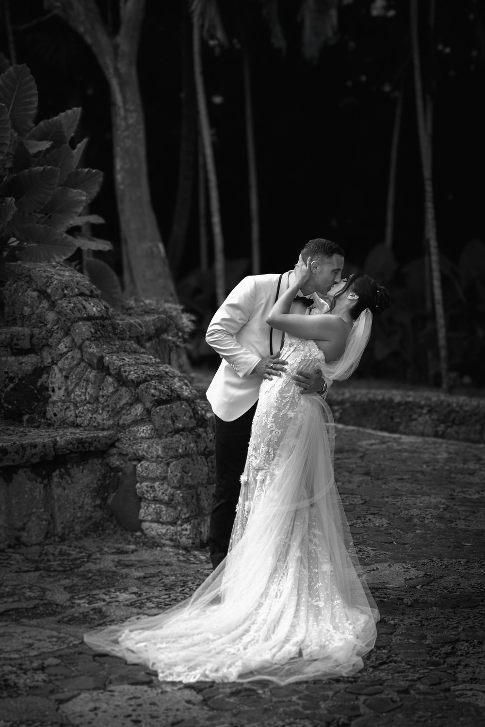 A romantic black and white wedding photo series showing a couple dancing and dipping in an outdoor garden setting.