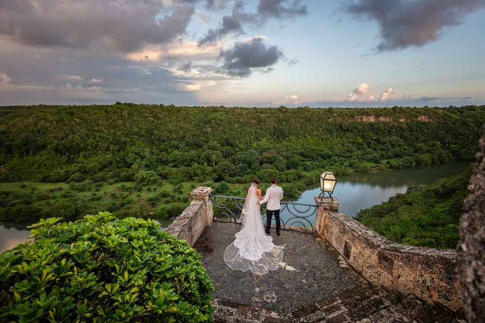 Scenic overlook at sunset with people standing on a rocky cliff above a winding river surrounded by lush greenery.