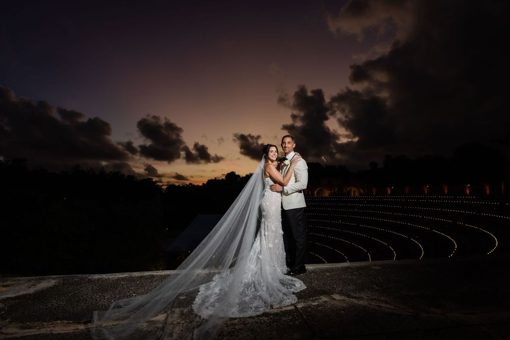 A couple in wedding attire embraces at dusk with dramatic storm clouds in the background creating a moody silhouette.