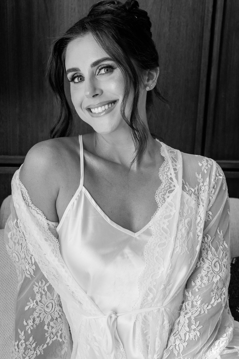 Black and white portrait of a smiling brunette woman in elegant white lace robe and satin slip dress.