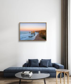 Warm gold framed photo print of the Twelve Apostles at sunset above a blue sofa in a white room.