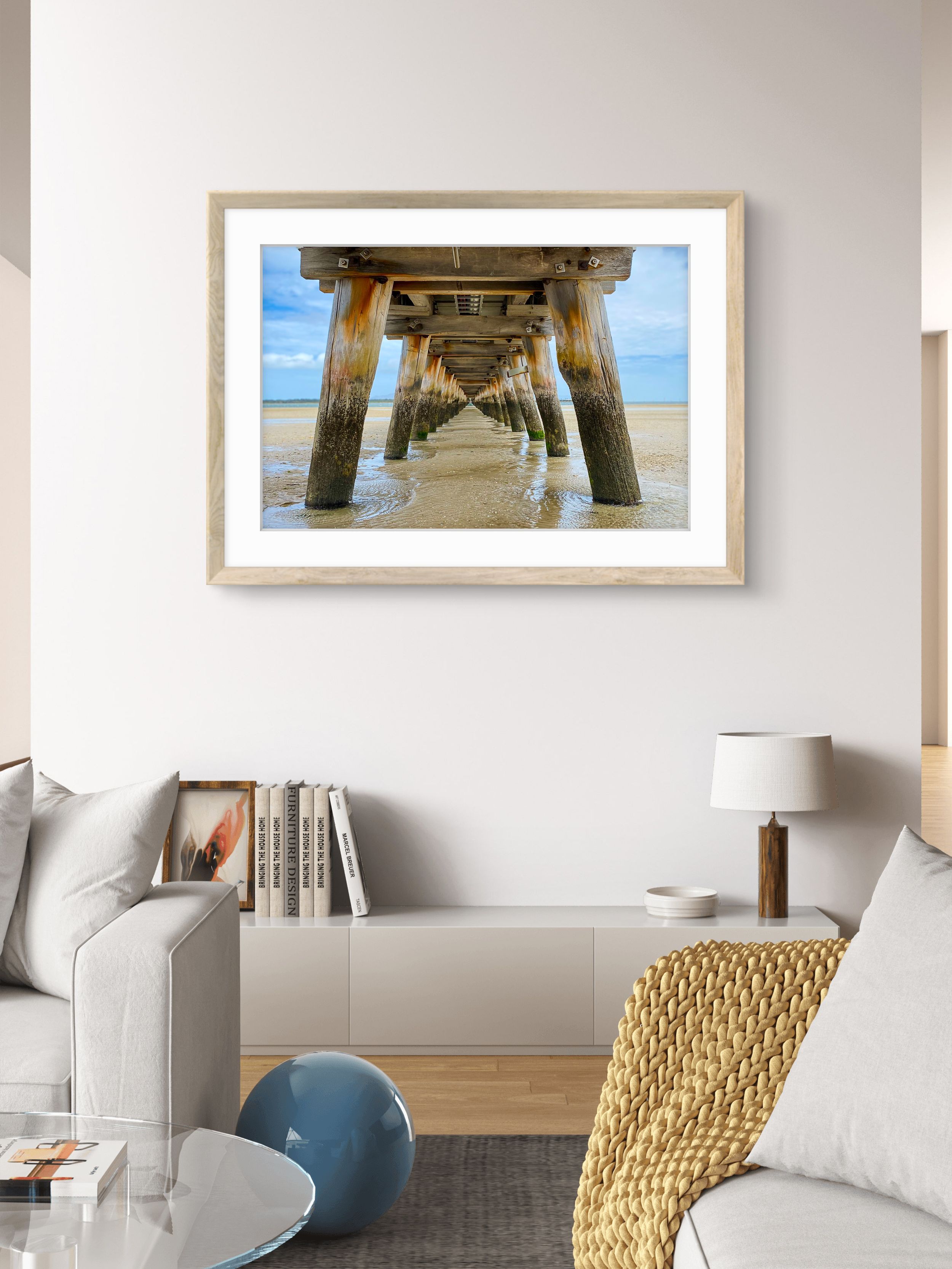 Framed photo of a beach pier's underside with symmetrical wooden pillars, displayed in a bright modern living room.