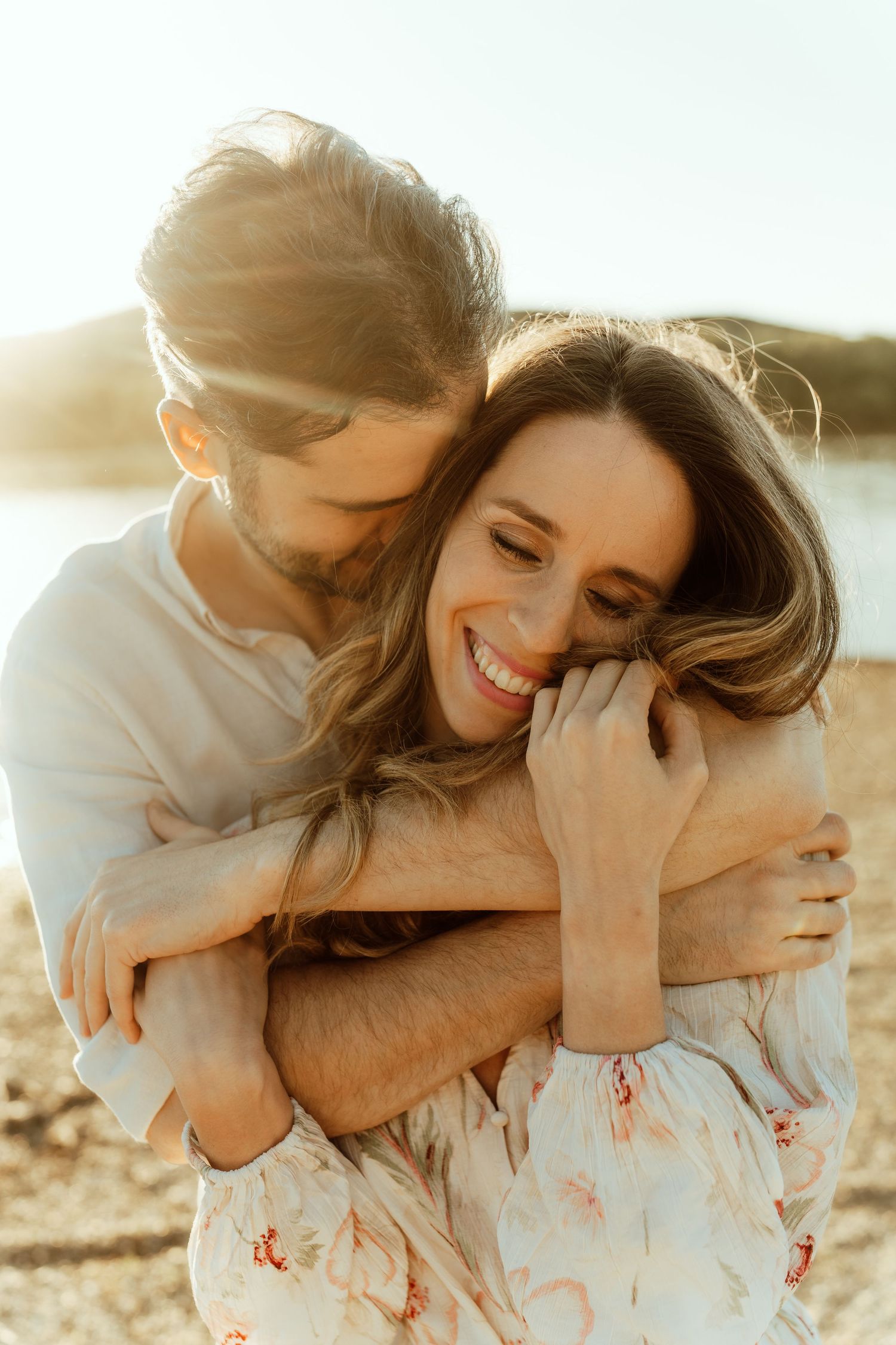 A romantic golden hour wedding photo of a couple embracing outdoors with soft sunlight illuminating their intimate moment.