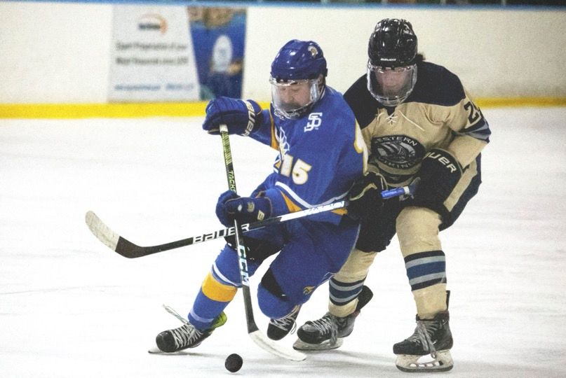 Two hockey players battle for the puck during an intense ice hockey match between blue and black uniformed teams.