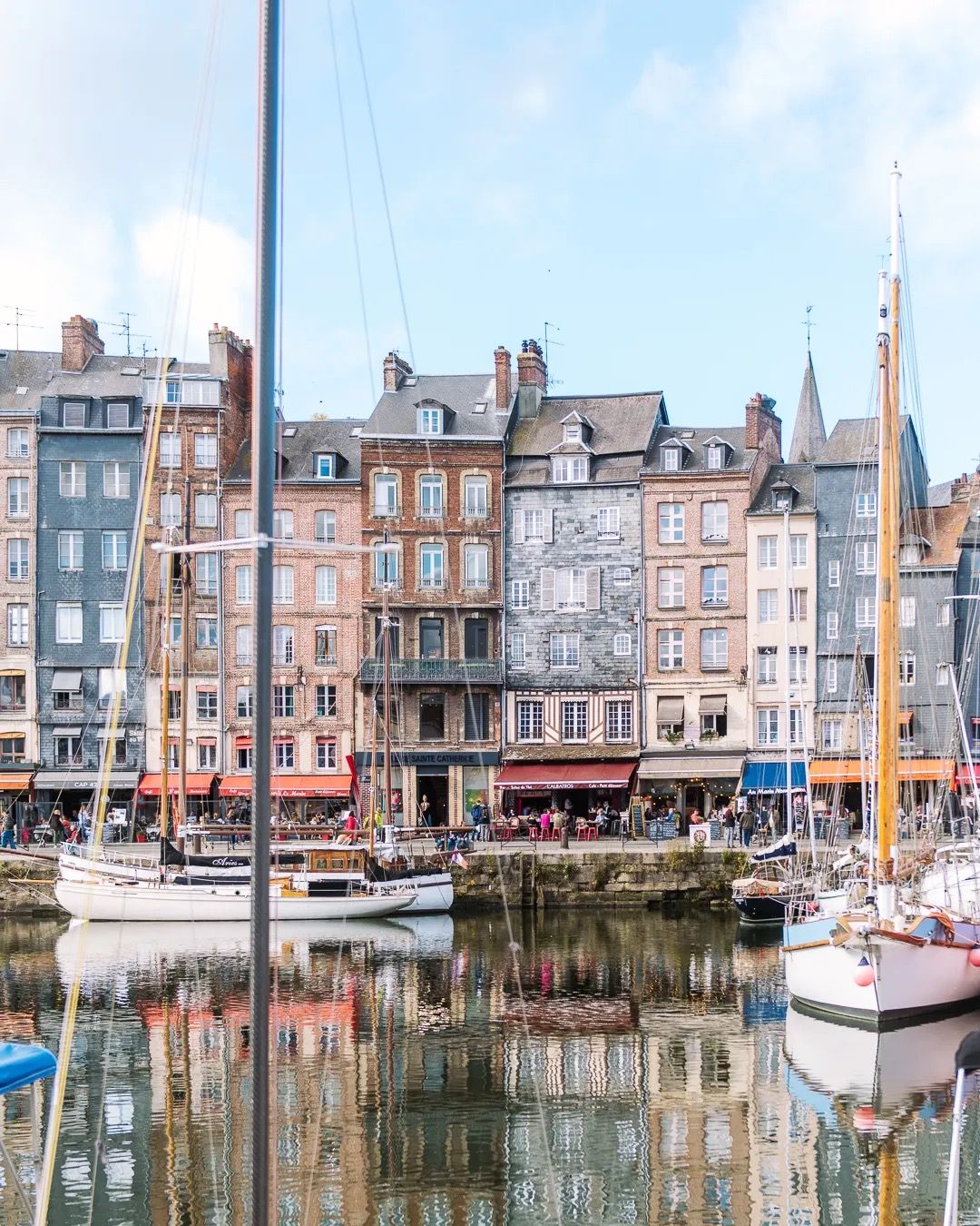 Harbour scene with colourful waterfront buildings and boats reflected in calm water.