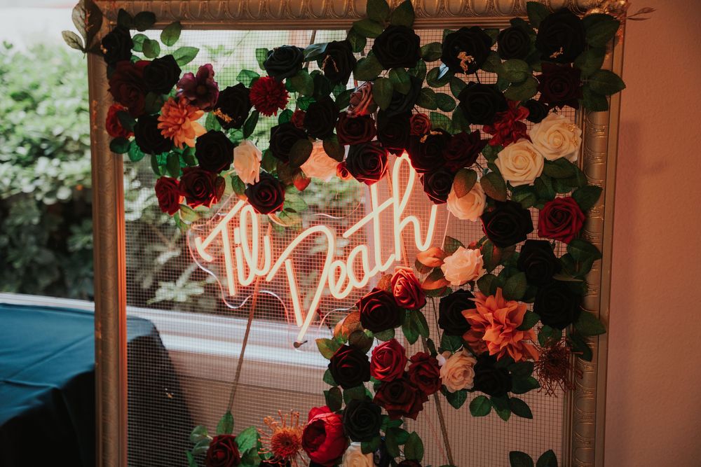 Neon 'Let's Party' sign glows above floral arrangements with pink and red roses against a wooden backdrop.